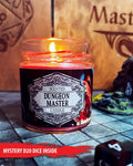 A lit scented candle in a clear glass jar labeled 'Scented Dungeon Master Candle' sits on a stone-tiled surface with a wooden background and gaming-themed props, including a red banner reading 'Mystery D20 Dice Inside'.
