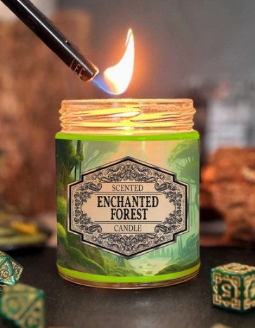 A lit scented candle in a clear glass jar with a green and black label reading 'Enchanted Forest Candle,' shown with a lighter igniting the flame against a dark, atmospheric background.