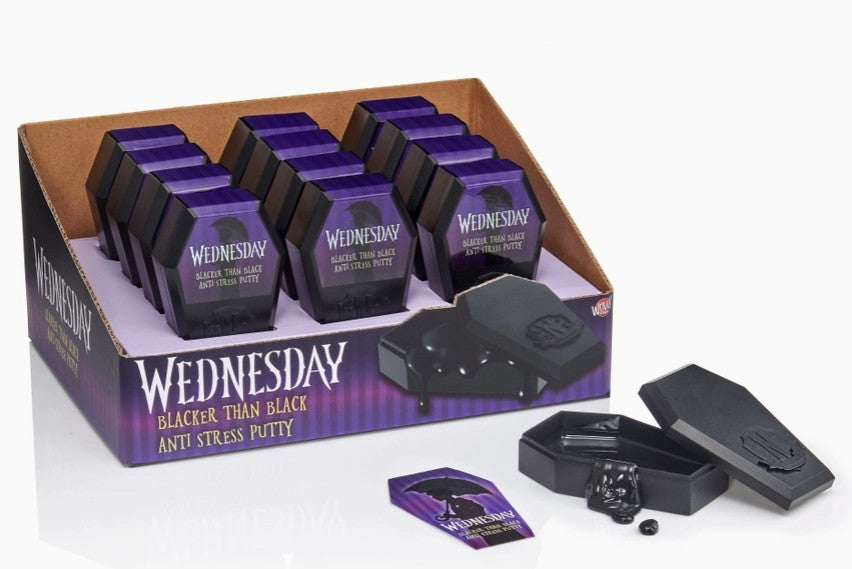 A display box of Wednesday Blacker Than Black Anti Stress Putty, showing multiple purple and black wrapped units inside, with one opened to reveal the black putty and small black container, plus a single loose packet in front on a white background.